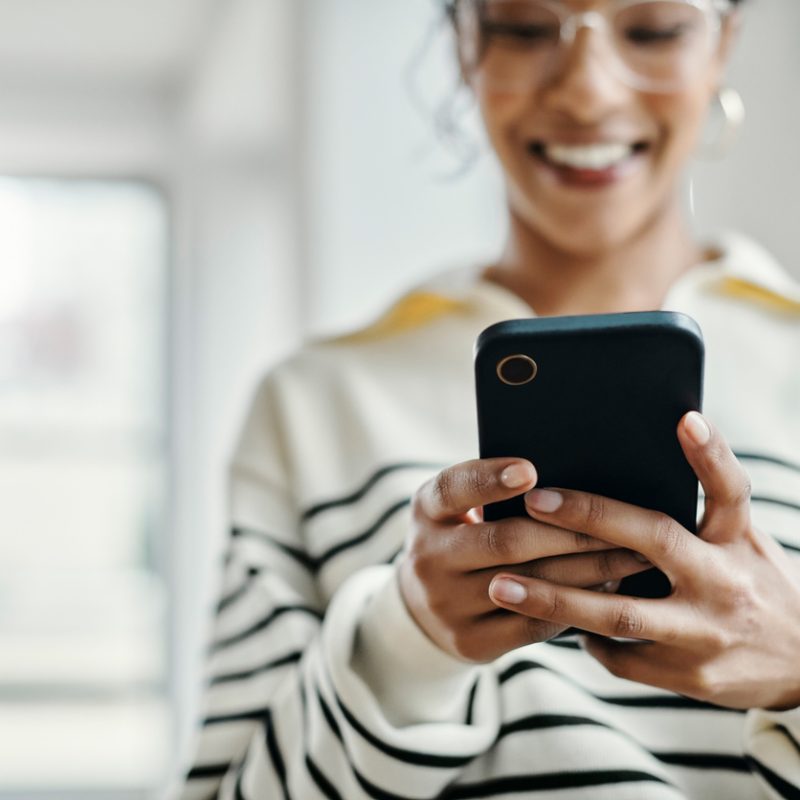 Woman, hands and phone with smile for communication, texting or chatting with technology at home. Hand of happy female smiling and enjoying social media, connection or browsing on mobile smartphone